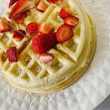 Picture of waffles with cut strawberries and maple syrup being poured on it