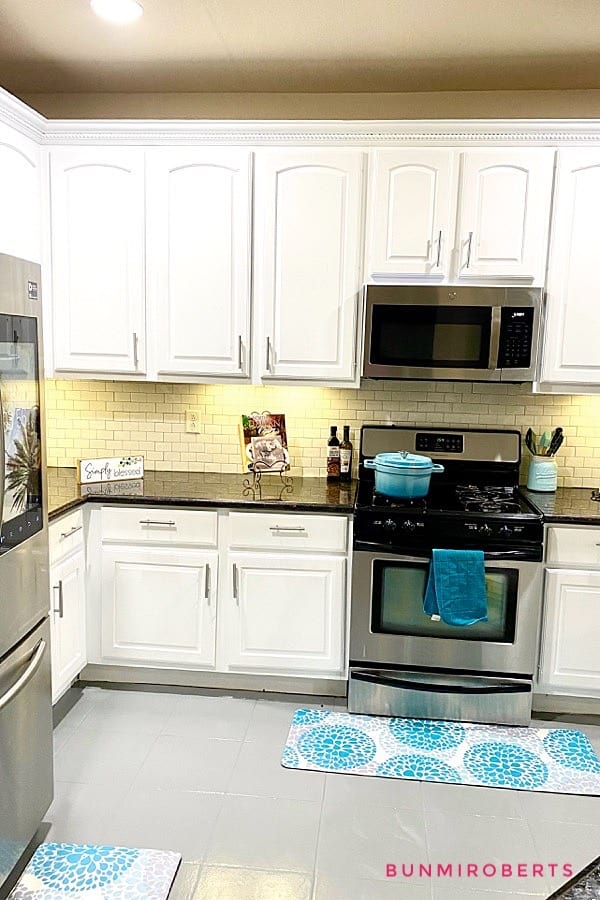 a kitchen with white cabinets, grey tile floor and white backsplash with a refrigerator