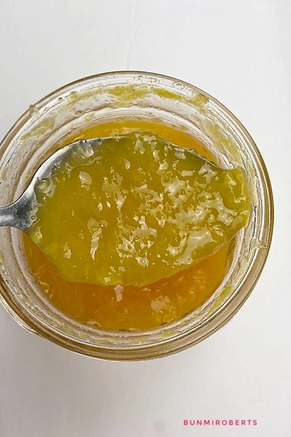 Orange jam in a jar being scoped with a spoon