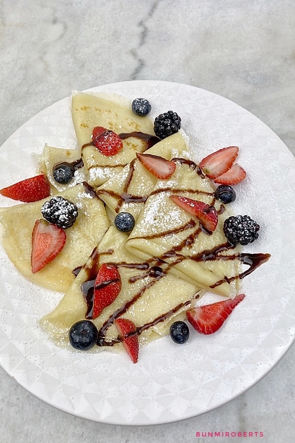 Crepes folded in quarters served with strawberries, blueberries, chocolate syrup and powdered sugar